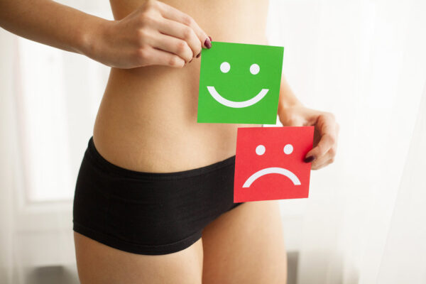 Woman Health Problem. Closeup Of Female With Fit Slim Body In Panties Holding Two Card With Sad Smiley And Happy Face Near Her Stomach. Digestive Disorders, Period Pain, Health Issues Concept.