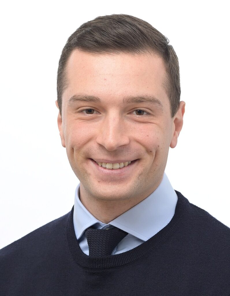 Portrait officiel de Jordan Bardella en costume, mettant en avant sa stature et son image publique